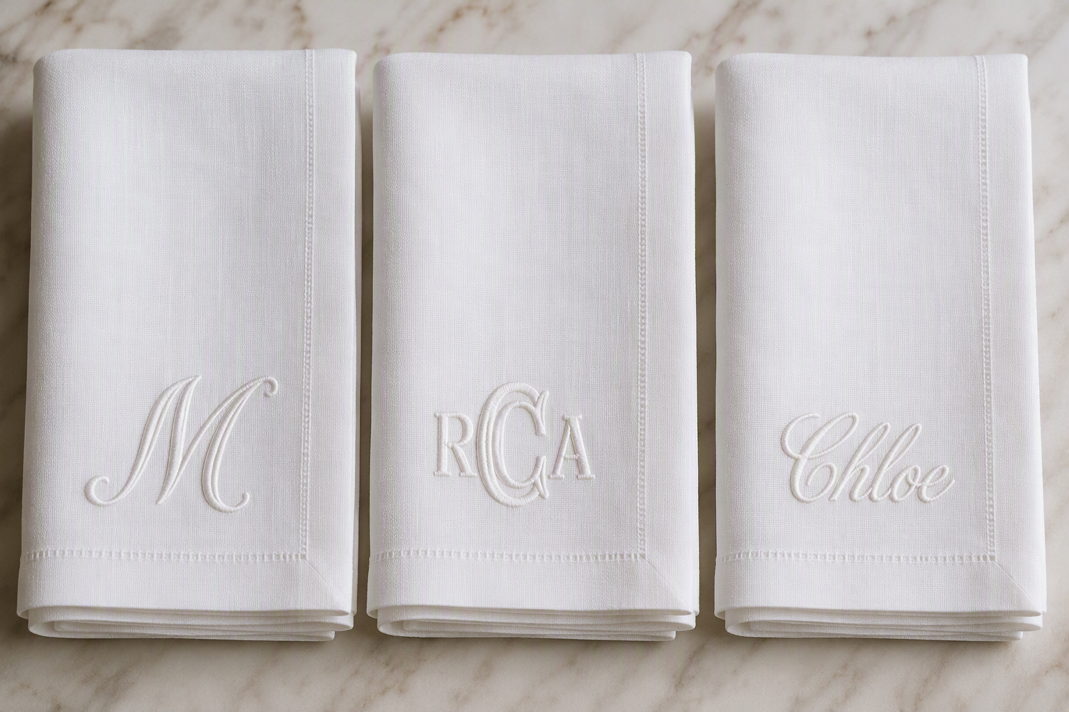 Three napkins showing different monogram styles: single initial, three-letter monogram and script name