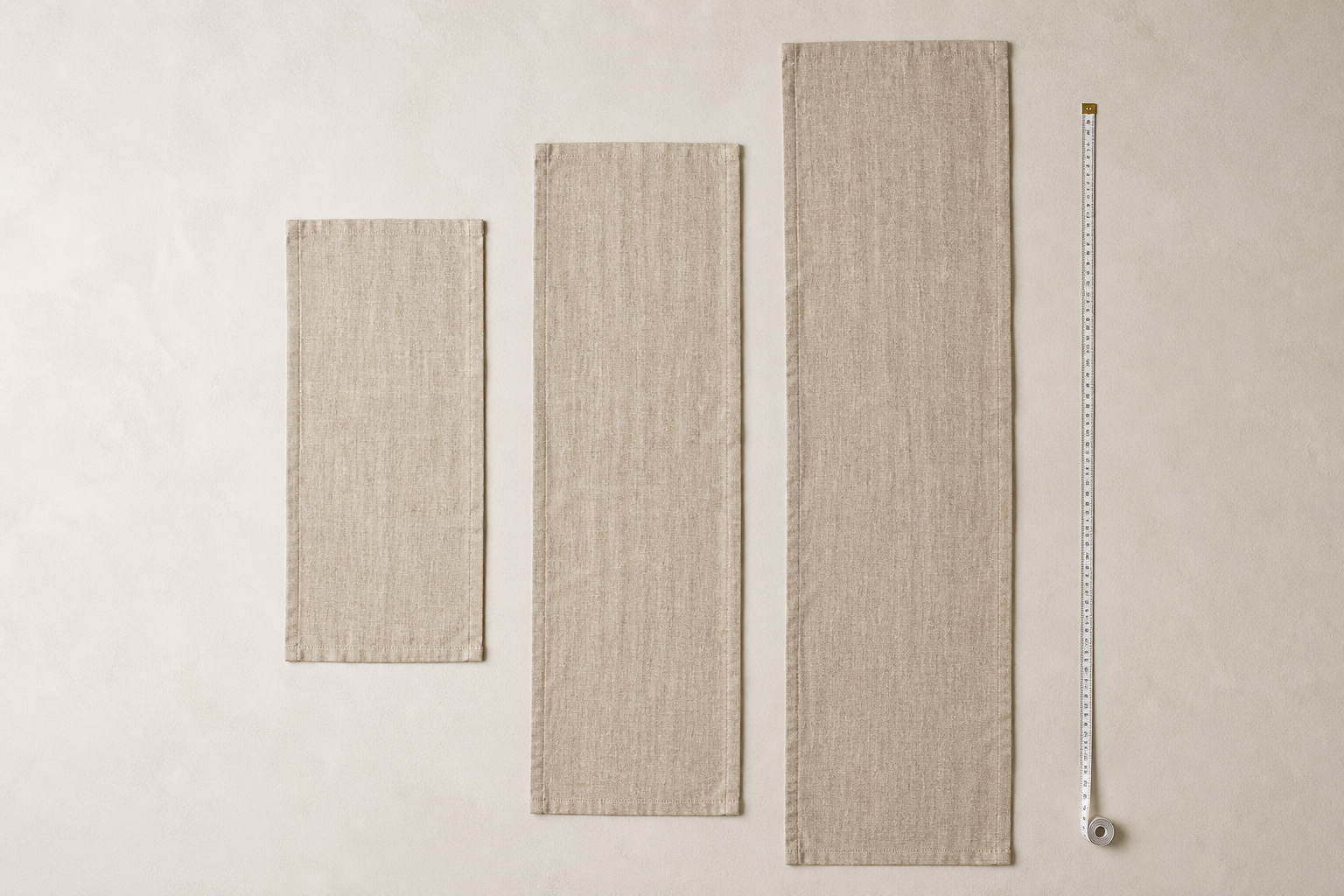 Three linen table runners of different lengths laid flat in a row with a measuring tape