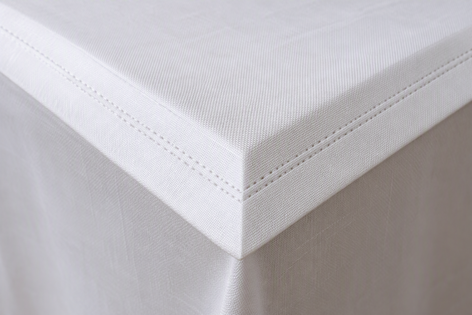 Macro close-up of a neatly mitered corner on a white woven tablecloth with clean stitching