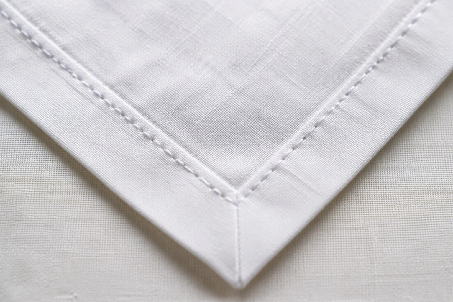 Macro close-up of a mitered corner on a white cloth napkin with clean double stitching
