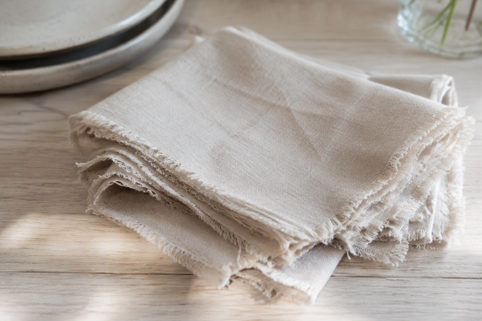 Natural linen napkins with raw unhemmed frayed edges folded on a wooden table