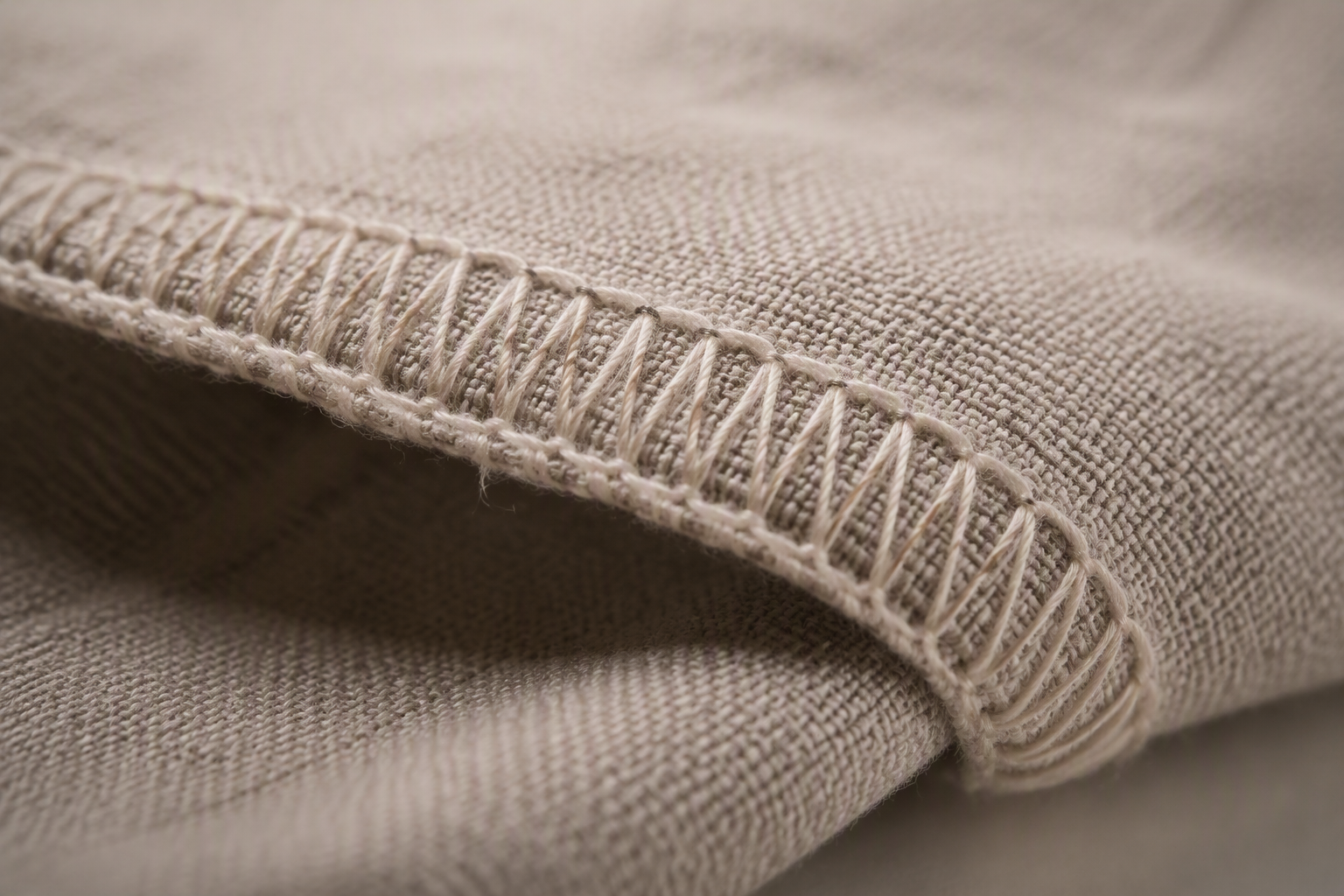 Close-up of the serged overlocked edge of a beige cloth napkin with visible zigzag stitching