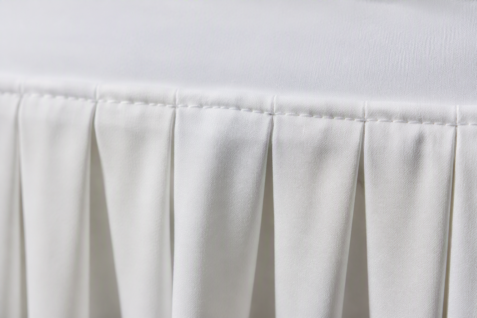Macro close-up of top-edge stitching holding the pleats of a table skirt in place