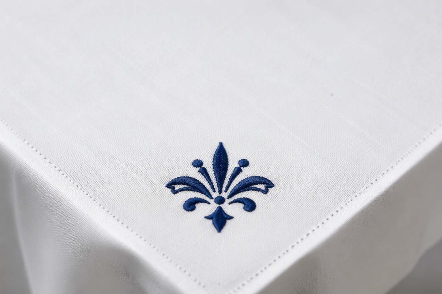 A tablecloth corner with a neatly embroidered emblem in deep navy thread