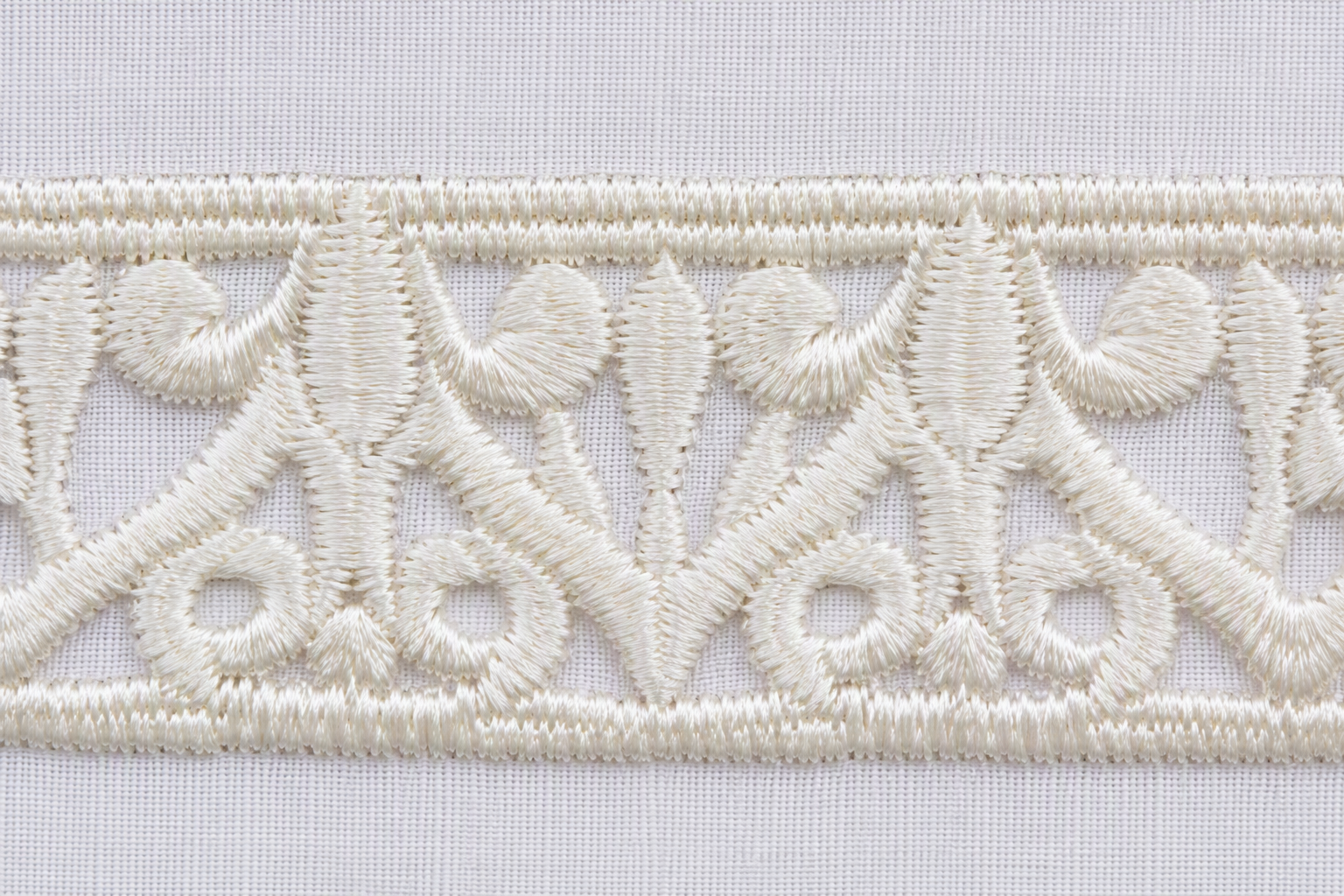 A dense satin-stitch embroidered border in ivory thread on white tablecloth