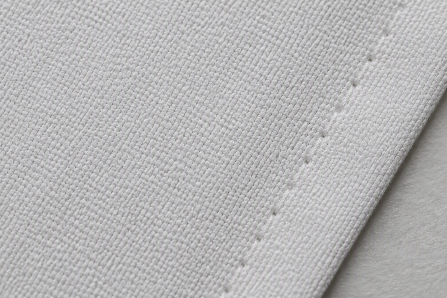 A macro close-up of white cotton napkin fabric, a tight even plain weave with a hem stitch along the edge