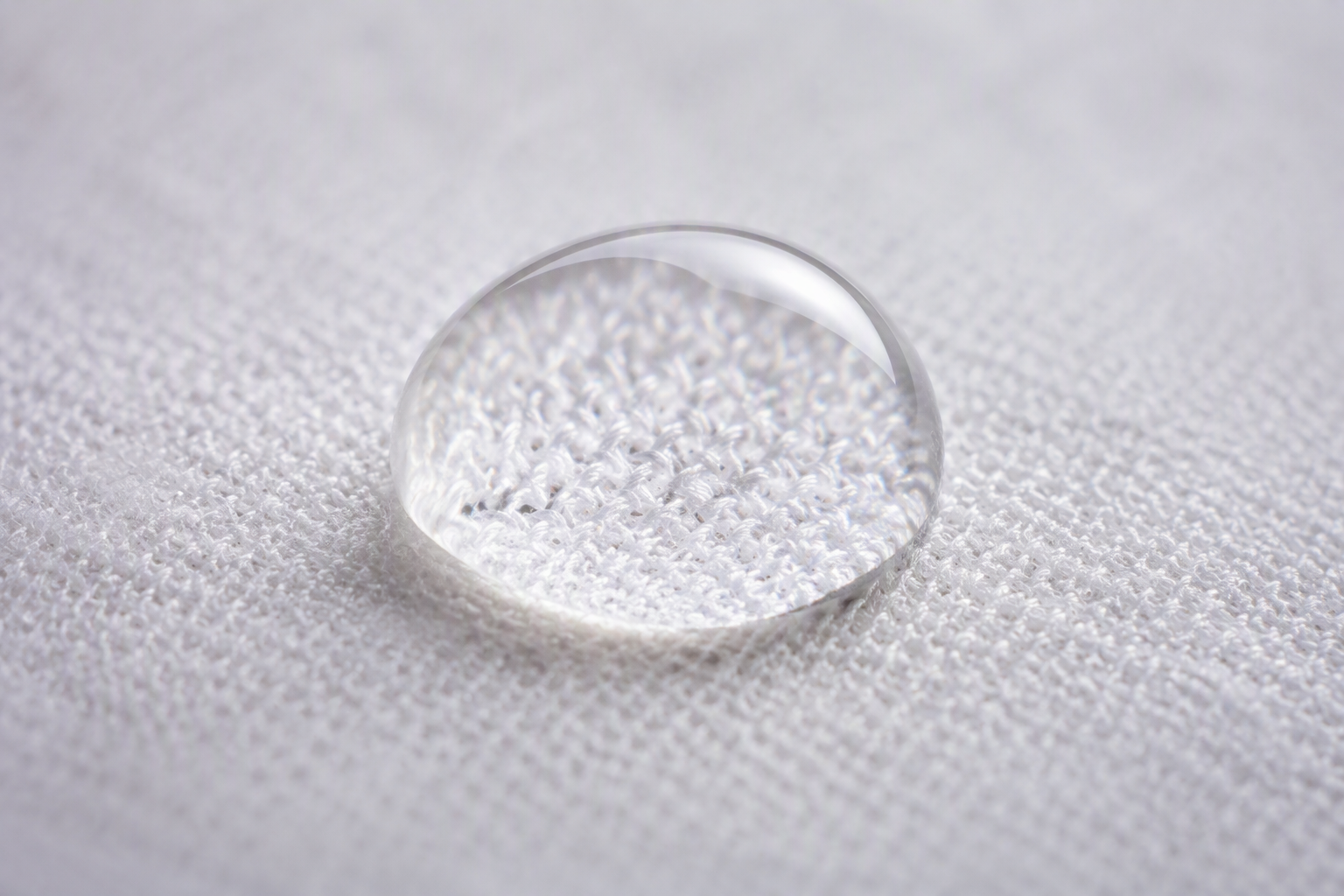 A clear water droplet beading into a sphere on the surface of a white fabric