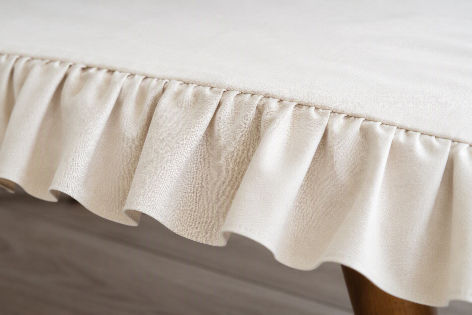 The ruffled edge of a cream cotton tablecloth with clean gathered folds