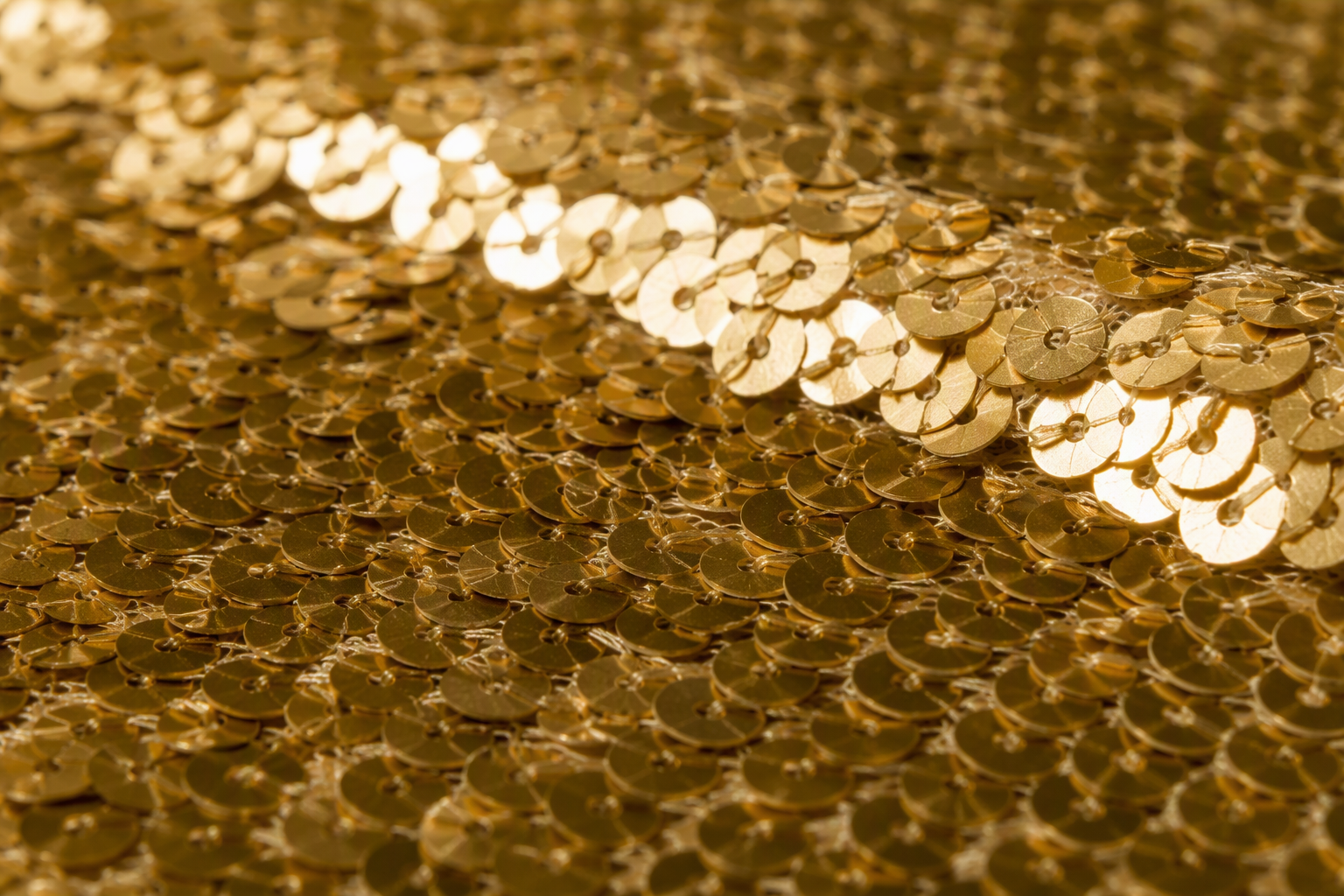 Macro of gold sequin fabric with small sequins densely stitched onto a mesh backing