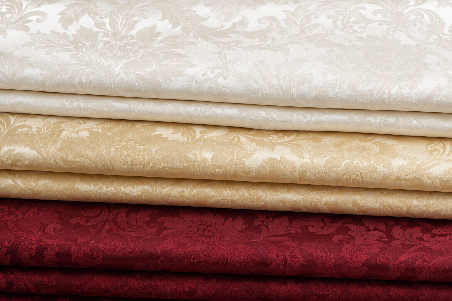 Damask tablecloths stacked in ivory, champagne and burgundy colourways